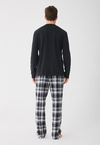 Chemise noire à manches longues associée à un pantalon de pyjama gris et noir à carreaux. Tissu doux, coupe décontractée et ourlet ouvert sur les pantalons.