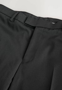 Pantalonii negri, tăiați, au o textură netedă, un front plat cu pliu, bucle pentru curea și o închidere cu fermoar la talie.