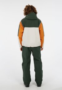 Kleurgeblokte jas met groene, witte en oranje panelen; met capuchon; elastische manchetten; gecombineerd met bijpassende groene broek; waterdicht materiaal.