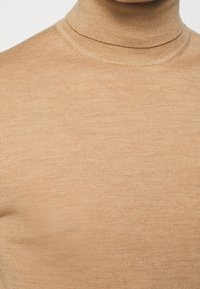 Pull en col roulé marron clair en tissu côtelé, avec un design ajusté et une texture lisse.