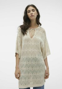 Gebreide tuniek in crème met een zigzagpatroon, met een diepe V-hals en strikdetail, oversized mouwen en een gestructureerde afwerking.