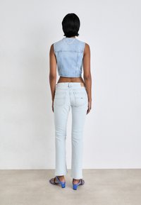 Chaleco de mezclilla recortado azul claro combinado con jeans ajustados azul claro. La modelo lleva sandalias de tacón azul. Texturas suaves y diseño casual.
