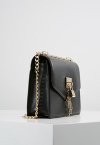 Borsa a mano in pelle nera con una forma strutturata, tracolla in catena dorata e dettaglio a lucchetto. Presenta una superficie liscia e un fermo prominente.