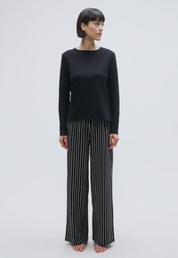 Haut noir à manches longues avec un col rond, associé à un pantalon large rayé noir et blanc. Tissu doux, coupe décontractée, sans motifs ni accents visibles.