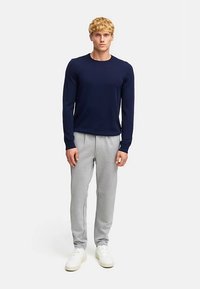 Mörkblå långärmad tröja tillsammans med ljusgrå mjukisbyxor och vita sneakers. Slät tyg, figurnära design och enkel färgpalett.