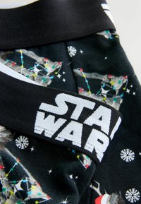 Czarna tkanina z wielokolorowym wzorem Star Wars, featuring światła, płatki śniegu oraz białą elastyczną taśmę w pasie z napisem "STAR WARS" wydrukowanym na bold.