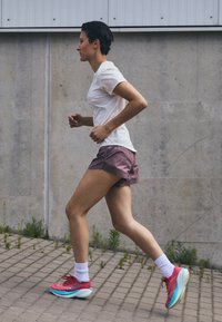 Sportos öltözet, amely magában foglal egy szabott fehér pólót, lila sortot hajtott szegéllyel és rózsaszín futócipőt világoskék részletekkel.