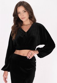 Schwarzes samtiges Cropped-Top mit V-Ausschnitt und Puffärmeln, kombiniert mit einem passenden, hoch taillierten Rock mit dekorativen Knöpfen.