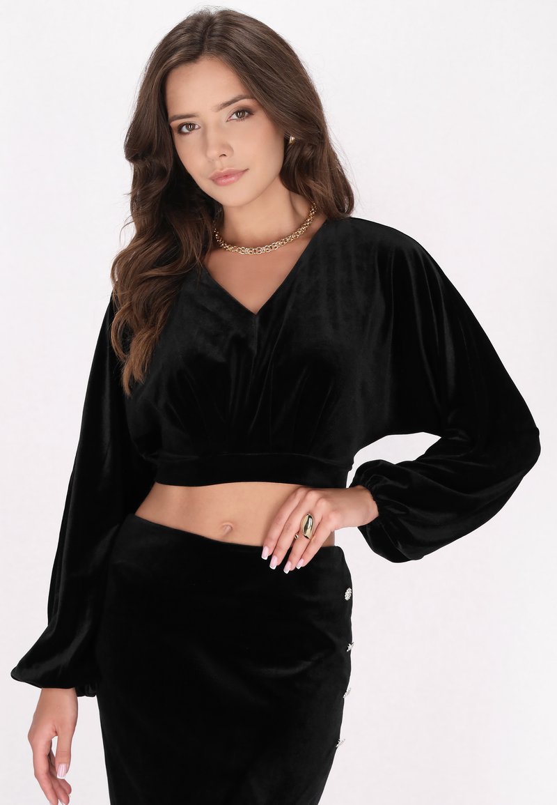 Schwarzes samtiges Cropped-Top mit V-Ausschnitt und Puffärmeln, kombiniert mit einem passenden, hoch taillierten Rock mit dekorativen Knöpfen.