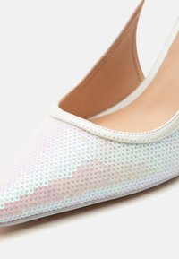 Λευκό παπούτσι με μυτερή μύτη με ουράνιες παγιέτες και λείο μπεζ εσωτερικό επένδυμα.