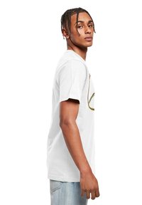Hvid bomulds T-shirt med korte ærmer, prydet med et farverigt abstrakt design på forsiden. Båret med lyseblå denim jeans.