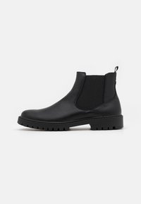 Bottines Chelsea en cuir noir avec des panneaux élastiques sur les côtés, une sangle de traction et une semelle robuste avec un profil cranté. Texture lisse avec un minimum de détails.
