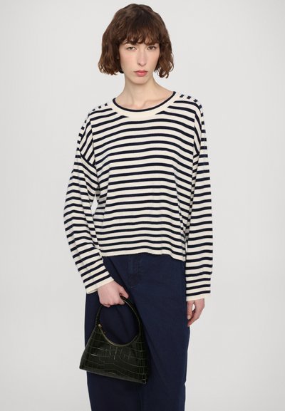 Maglione a righe in crema e blu navy, con ampia scollatura rotonda e vestibilità ampia. Abbinato a una piccola borsa nera con motivo coccodrillo.
