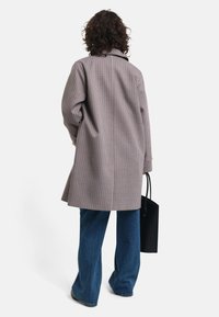 Houndstooth-frakke i brun og creme, mellemlang med notch-krave, parret med brede blå jeans og en sort taske. Tekstureret stof.