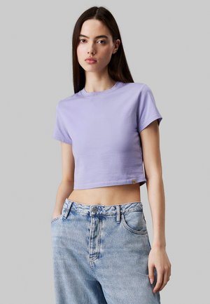 Lilla cropped t-shirt lavet af glat bomuld, med korte ærmer og rund halsudskæring. Bæres med højtaljede lyseblå jeans.