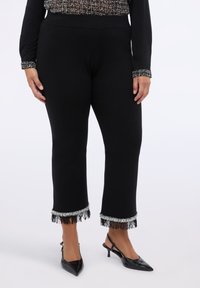 Černé zkrácené kalhoty s ozdobeným tř�ásňovým lemem a stříbrnými akcenty. Měkká, elastická tkanina; s špičatými černými podpatky.