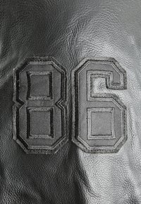Black leather material with textured surface, featuring embroidered numbers "86" in dark thread. Bold, geometric design with raised accents.