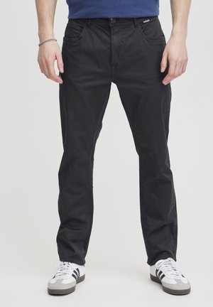 Black cotton trousers with a relaxed fit, featuring front pockets and a button closure. Worn with white sneakers and a blue top.