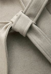 Beige wollen stof met een zachte, gestructureerde oppervlakte, voorzien van een geknoopte accentdetail en gevouwen randen.