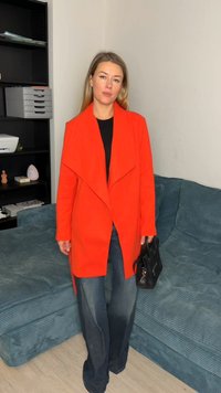 Bright orange jacket with a flowing open front design, paired with black top and blue wide-leg jeans. Holding a black bag.
