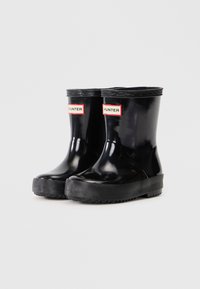 Bottes de pluie en caoutchouc noir avec une finition brillante, une semelle noir texturée et des étiquettes HUNTER à l'avant en rouge et blanc. Hauteur courte jusqu'à la cheville.