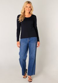 Marineblauwe lange mouwen top gecombineerd met ruime blauwe denim jeans. De outfit heeft een klassieke ronde halslijn en een ontspannen pasvorm. Zwarte sandaaltjes met hak.