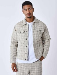 Mønstret beige denimjakke med geometrisk design, knaplukning, brystlommer og matchende bukser. Båret over en hvid t-shirt.
