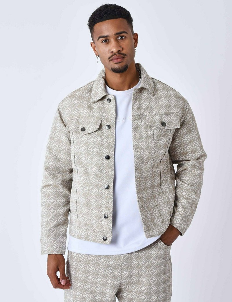 Mønstret beige denimjakke med geometrisk design, knaplukning, brystlommer og matchende bukser. Båret over en hvid t-shirt.