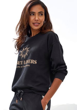 Black sweatshirt made of soft fabric, featuring a sun graphic and "SUNSET LOVERS" text in beige, with a relaxed fit and ribbed cuffs.
