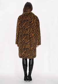 Bruine en zwarte gestreepte faux-fur jas met brede kraag, lange mouwen en een losse pasvorm, gecombineerd met glanzende zwarte leggings en laarzen met hakken.