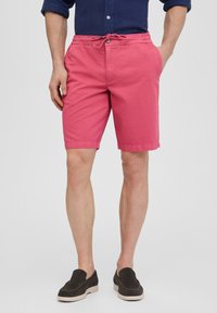 Shorts en coton rose avec une taille élastique et un cordon de serrage. Comprend des poches latérales et une coupe simple, associés à des chaussures slip-on sombres.