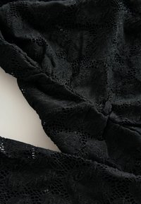 Czarna koronkowa tkanina z misternymi kwiatowymi wzorami i teksturowaną powierzchnią, z lekkim połyskiem i marszczeniami przy szwach.