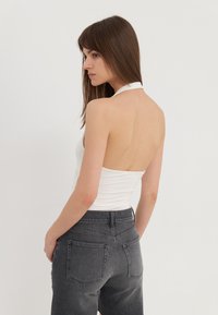 Bílý body s halter výstřihem a otevřeným zádem v kombinaci s tmavě šedými džínami s vysokým pasem. Hladká látka, minimalistický design a přesně vypracované švy.