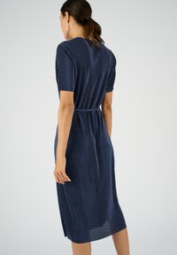 Vestido de marina con mangas cortas, cintura elástica, patrón de lunares, a la altura de la rodilla, tela ligera y aberturas laterales para mayor comodidad al moverse.