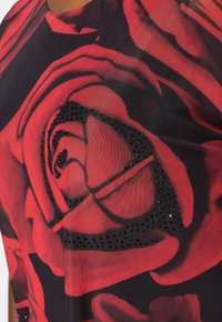 Top con motivo floreale che presenta rose rosse su uno sfondo nero, accentuato da borchie nere per aggiungere texture e dettagli. Tessuto leggero.