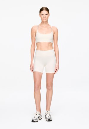 Zestaw sportowy w kolorze jasnobeżowym, składający się z dopasowanego topu i szortów o gładkiej fakturze. Noszony z srebrnymi sneakersami, w stylu minimalistycznym.