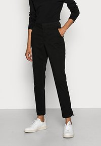 Pantalons noirs fuselés avec une texture lisse et un l�éger éclat, dotés de poches latérales et d'une coupe slim, associés à des baskets blanches.