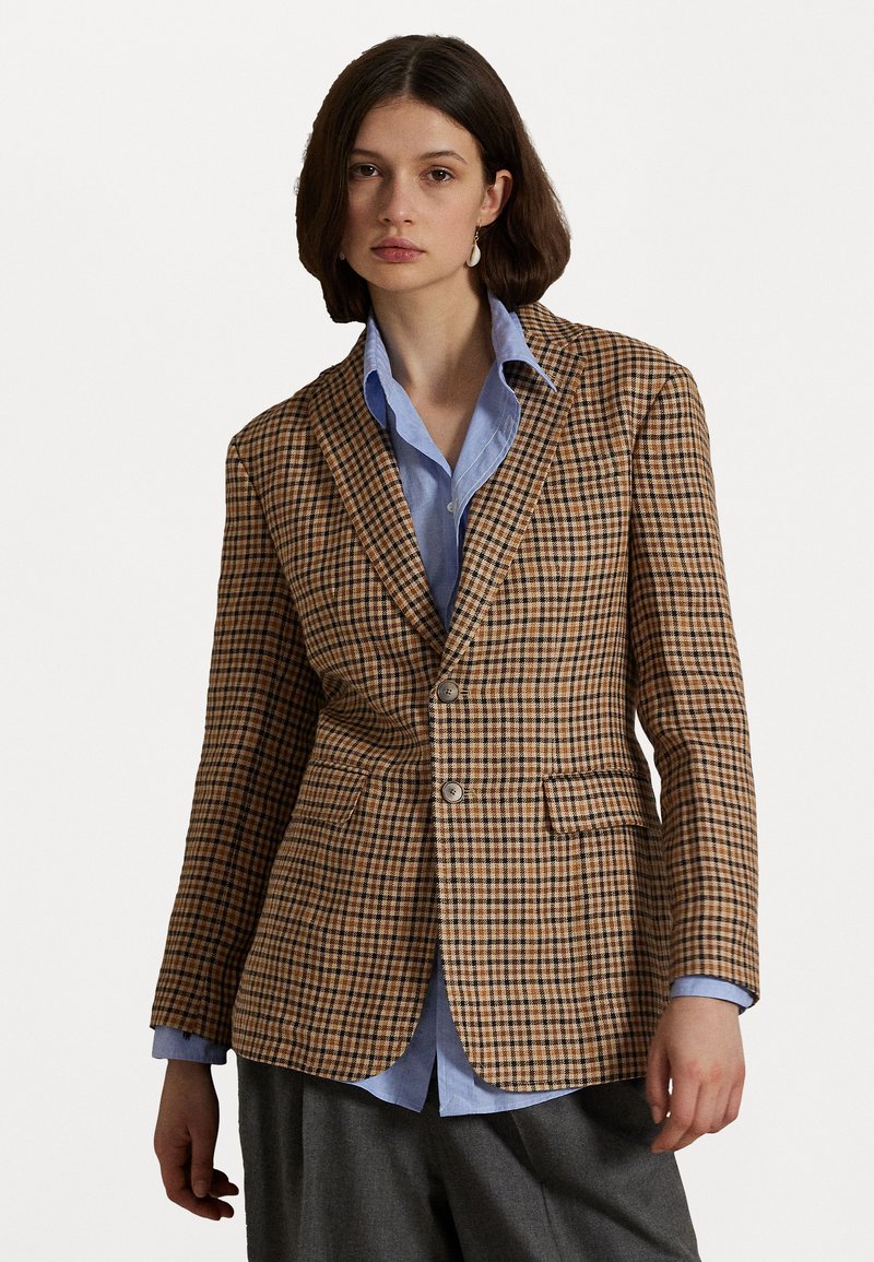 Bruine blazer met een ruitpatroon, gemaakt van gestructureerde stof, met een enkele knoopsluiting, notch revers en twee voorkruiden over een blauwe shirt.