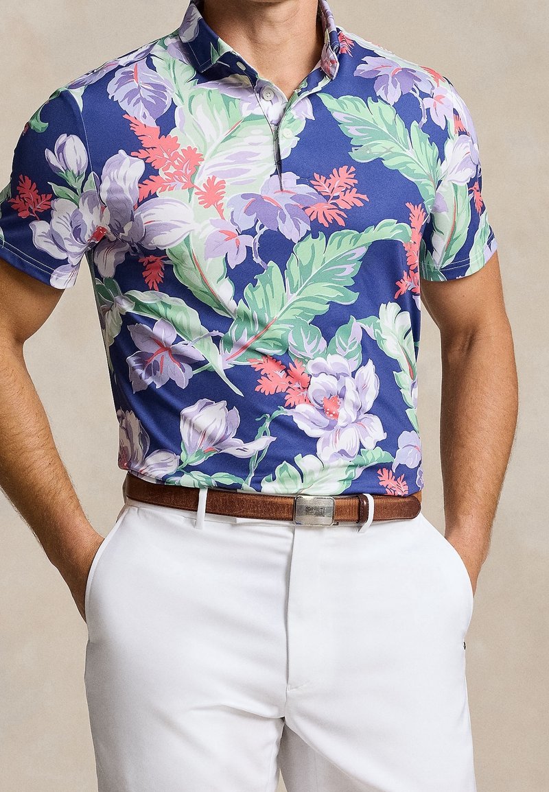 Polo a maniche corte di colore blu navy con un motivo floreale che presenta foglie viola, rosa e verdi. Realizzato in un tessuto liscio e traspirante.