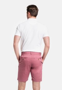 Chemise polo blanche à manches courtes, associée à un short rose avec deux poches arrière et des boutons.