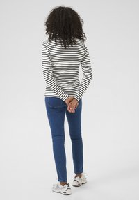 Gestreept top met lange mouwen in zwart en wit, gecombineerd met blauwe skinny jeans. Model draagt lichtgekleurde sneakers. Achteraanzicht weergegeven.