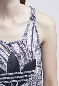 Black and white tank top featuring a floral pattern and a prominent black logo on the front, made from lightweight, breathable fabric.
