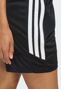 Μαύρο αθλητικό σορτς με τρεις λευκές ρίγες στο πλάι, κατασκευασμένο από λείο ύφασμα. Διαθέτει εφαρμοστό σχεδιασμό και ραμμένο τελείωμα.