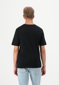 Zwarte katoenen t-shirt met korte mouwen, rechte zoom en ronde hals. Draagt het met lichtblauwe jeans. Geen patronen of opvallende accenten.
