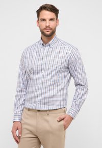 Geruit overhemd met knopen in blauw, wit en bruine tinten, met een kraag en lange mouwen. Gecombineerd met beige broek met een zijzak.