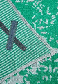 Green textured fabric featuring a striped and patterned design, with a gray stitched accent and a dark gray patch.