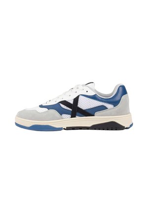 Zapatilla baja con parte superior de malla blanca y ante, acentos de cuero azul, rayas laterales negras y una suela de goma crema con dibujo azul y negro.