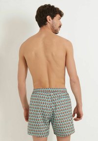 Uimashortsit miehille, joissa on vaaleansininen tausta ja toistuvat graafiset printit. Elastinen vyötärö, jossa on nappisulku.