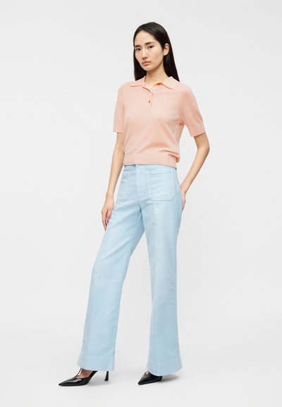 Ανοιχτό ροζ κοντομάνικο πόλο με κλασικό γιακά· συνδυασμένο με παστέλ γαλάζια παντελόνια φαρδιάς γραμμής με μπροστινές τσέπες και απαλή υφή.