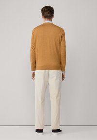 Sweter w kolorze musztardowym, wykonany z miękkiego materiału, z okrągłym dekoltem, zestawiony z jasnymi spodniami i ciemnymi sneakersami, widok z tyłu.